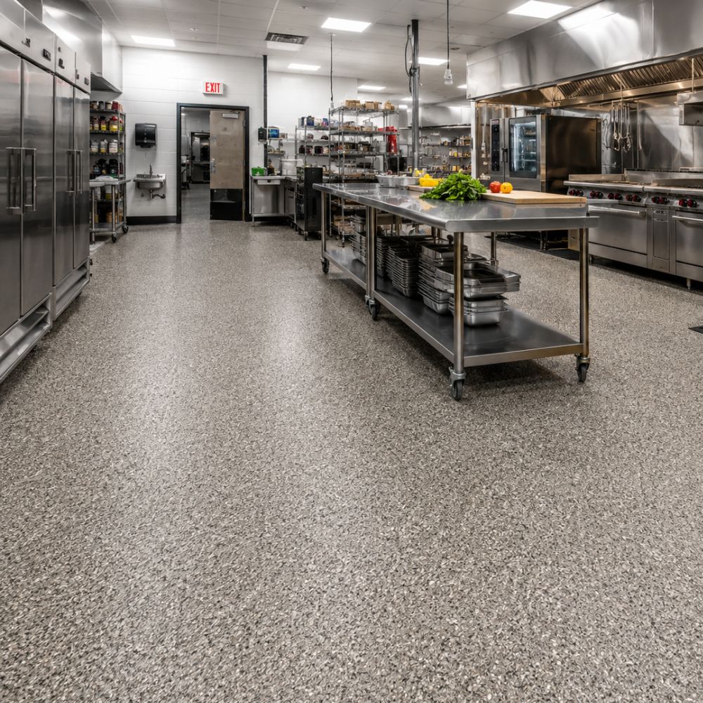 Large commercial kitchen with stainless steel prep island, metal shelving, and rows of appliances under bright overhead lights; vegetables on cutting board at center.