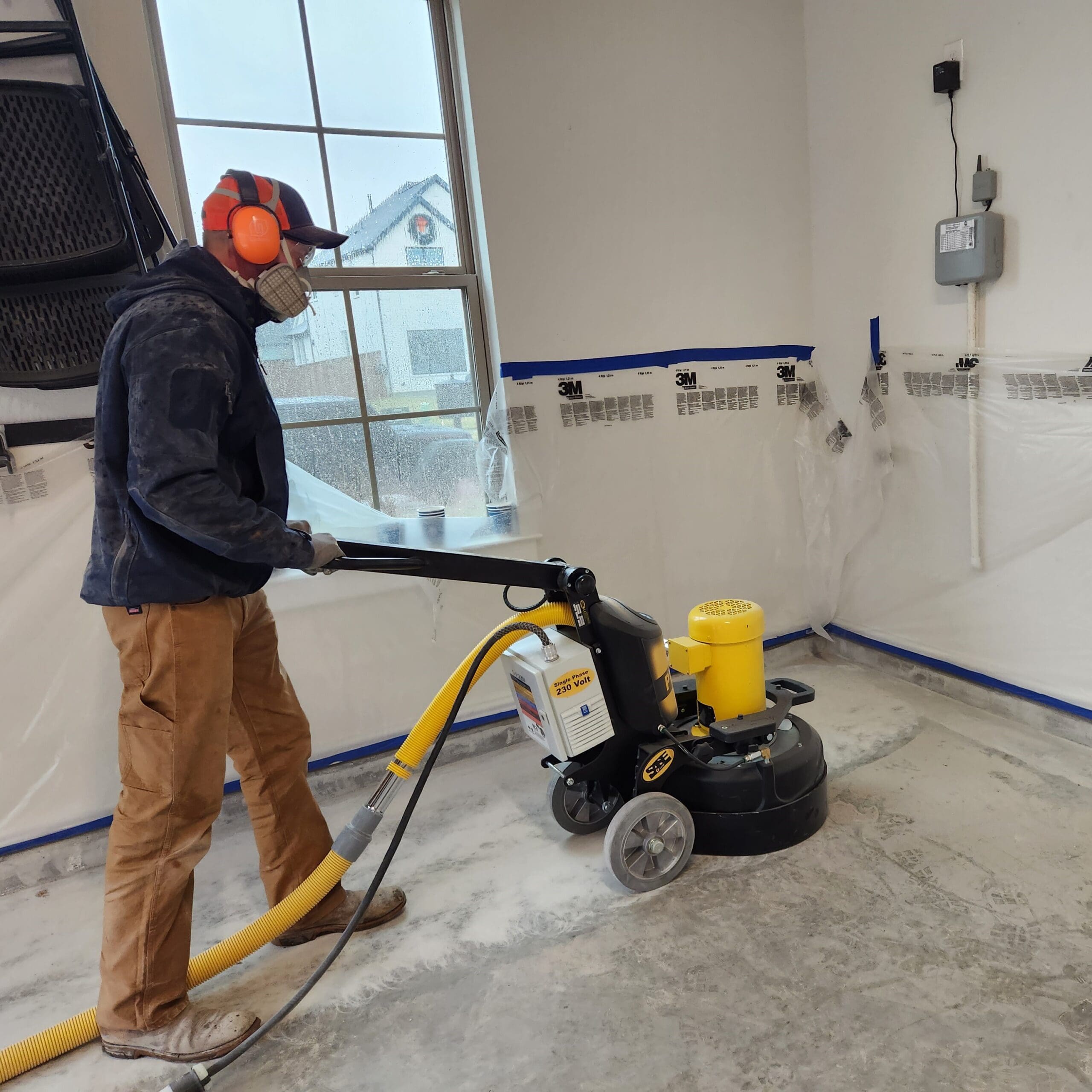 A MyGarageFloors installer running a diamond grinder across a garage slab to open the concrete before the polyaspartic base coat