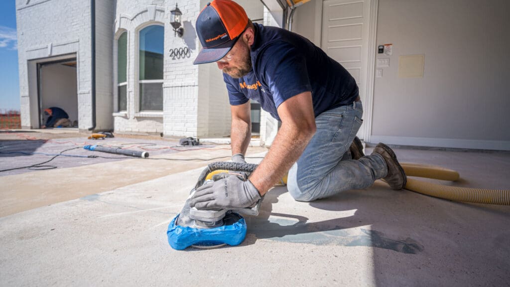 An installer kneeling at a garage door opening to prep the bare concrete slab