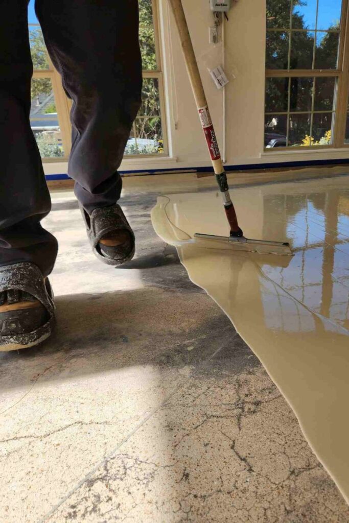Worker applying garage floor paint with a squeegee.