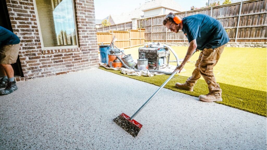 Two installers broadcasting color flake across a covered patio floor coating, one working the wet surface