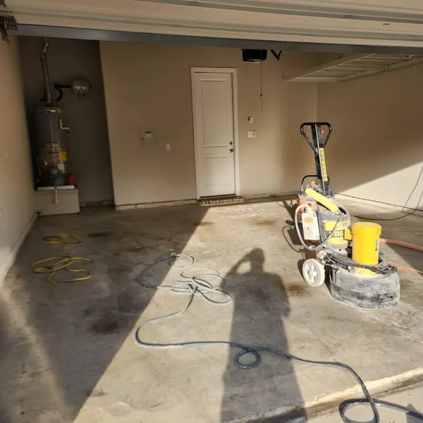Stained concrete garage floor being ground down before coating, with the grinder still on the slab