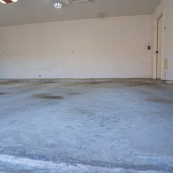 Bare gray concrete garage floor before coating, in an empty garage with plain white walls