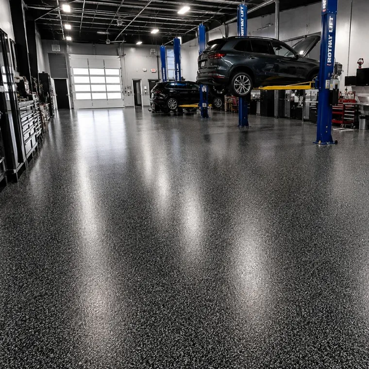 Auto service bay with two vehicles raised on blue lifts above a dark charcoal flake polyaspartic floor reflecting the overhead lights
