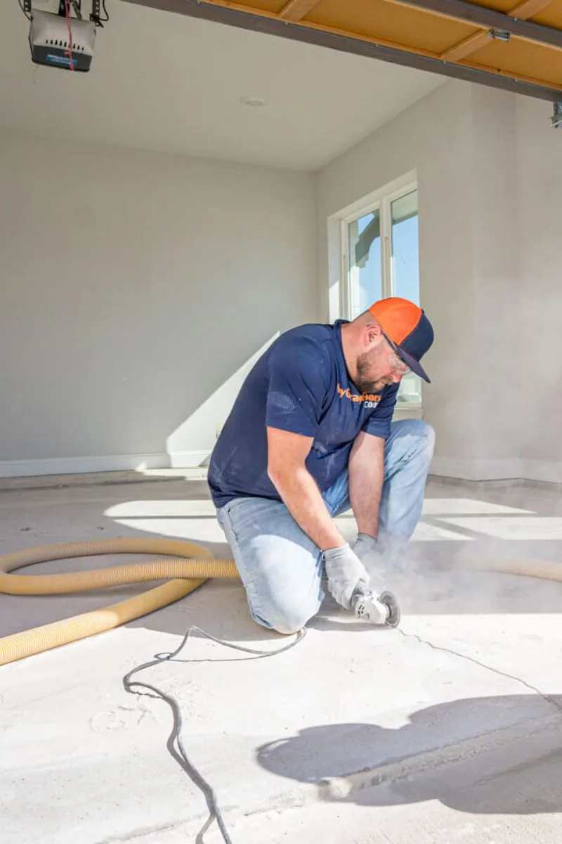 An installer grinding the edge of a bare concrete floor with a hand grinder