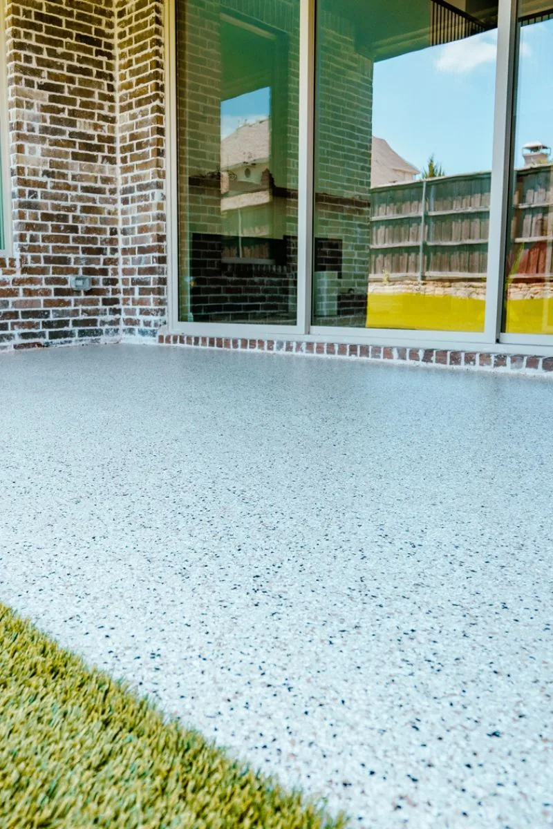 A light blue and white flake floor on a covered patio with a lawn and a fence beyond