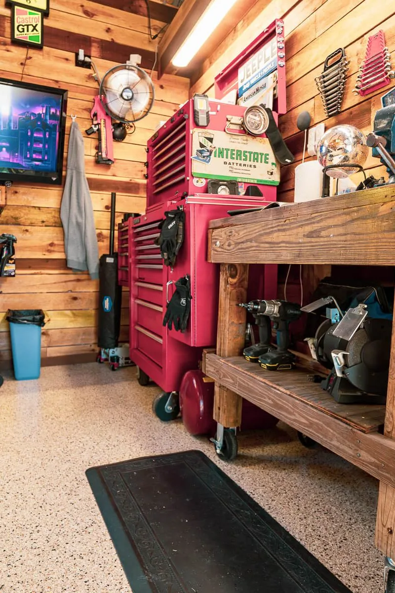 A garage workshop with a wood plank wall, a mounted TV, a red tool chest and a workbench