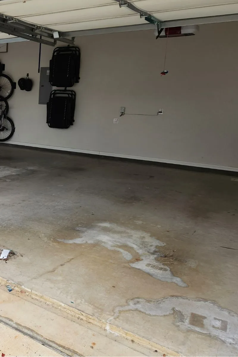 A bare concrete garage floor with dark stains spreading across the slab near the door