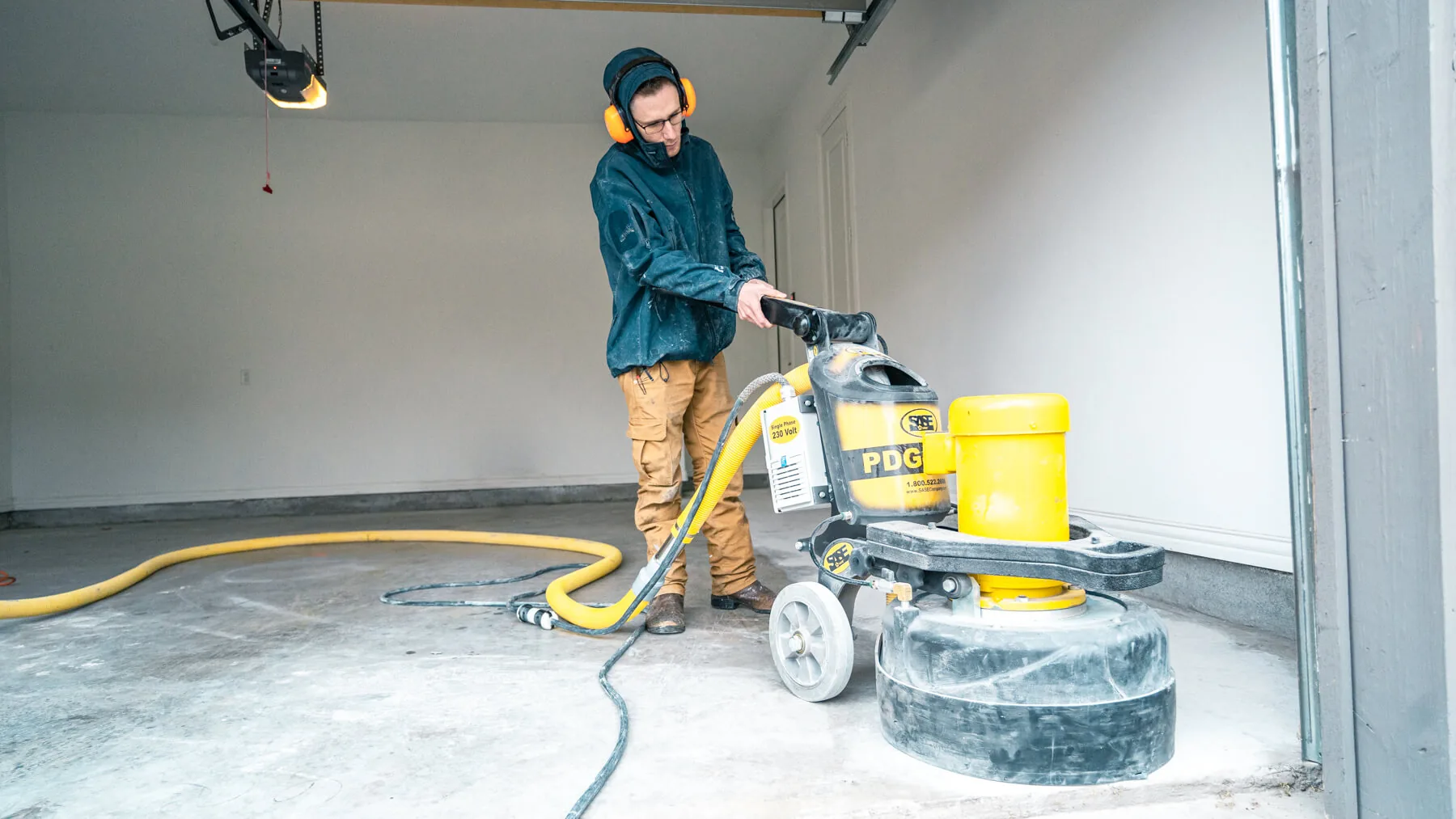 An installer grinding a bare concrete garage floor with a walk behind diamond grinder