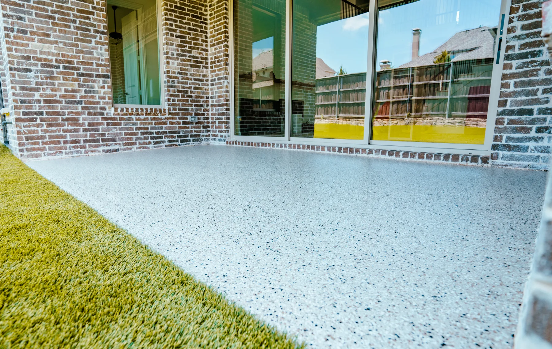 A light blue flake floor on a covered patio beside a brick house
