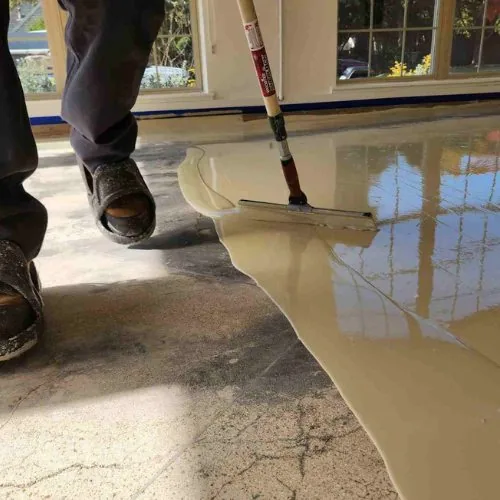 An installer spreading the base coat across bare concrete with a squeegee