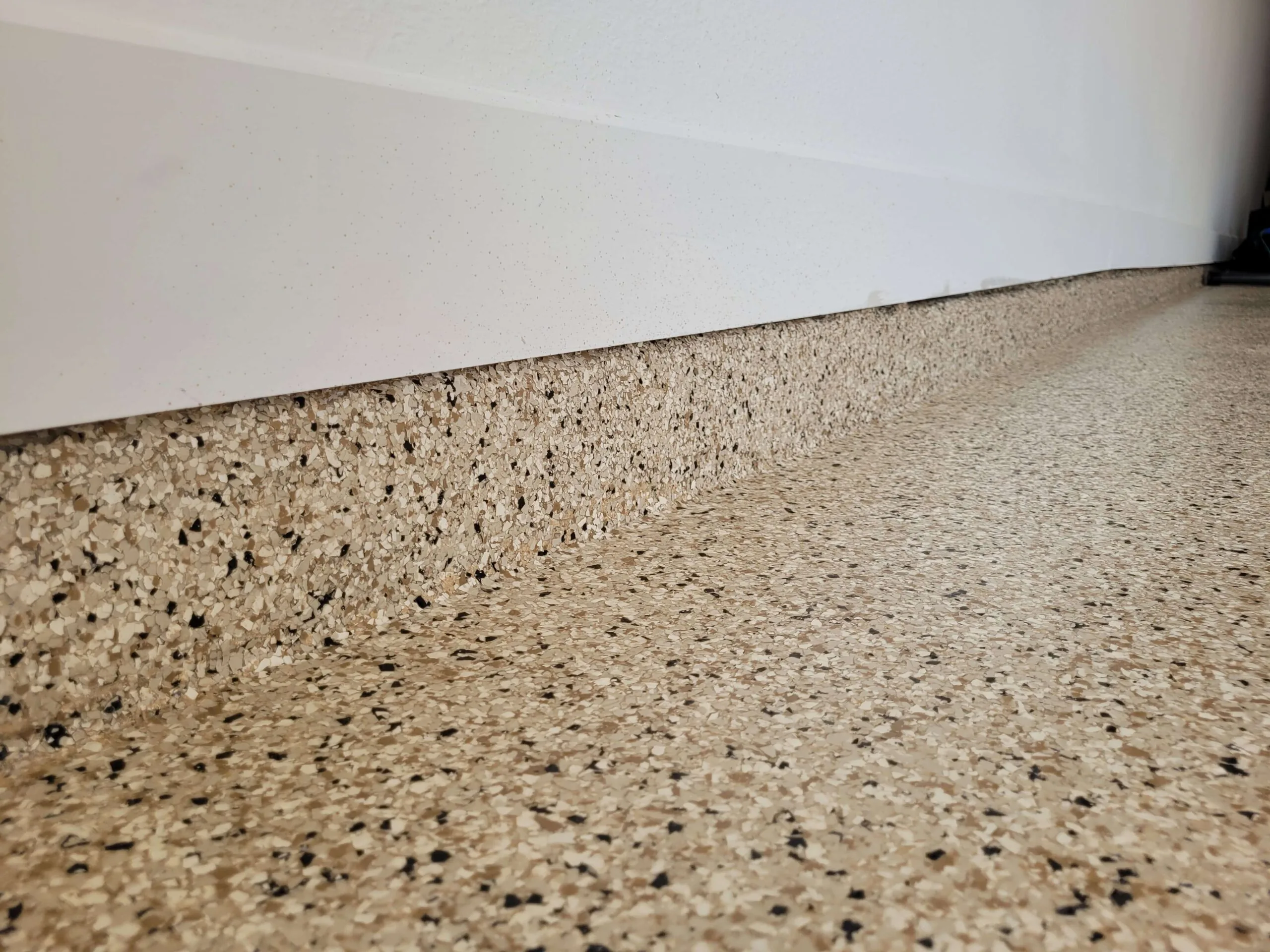 Close up of a tan and black flake floor where it meets the wall
