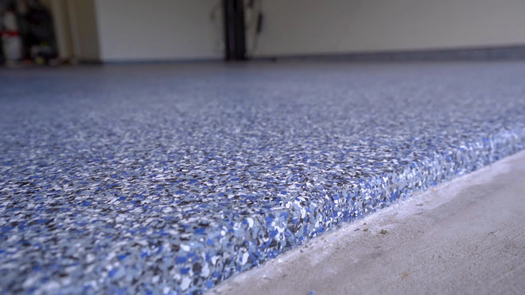 Close up of a finished blue gray flake floor meeting bare concrete at the door line