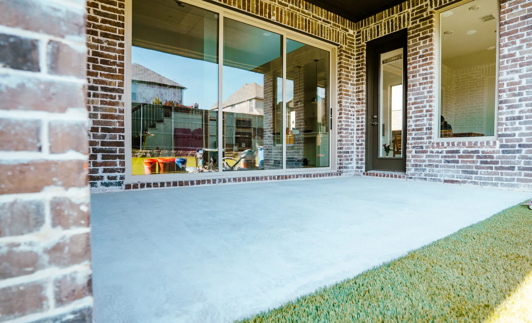 A coated back patio outside a brick house, beside a glass door