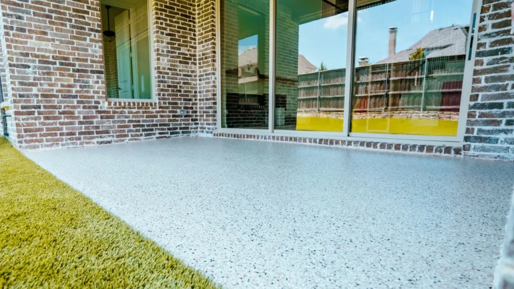 A covered patio finished in light blue and white flake polyaspartic coating next to a brick wall