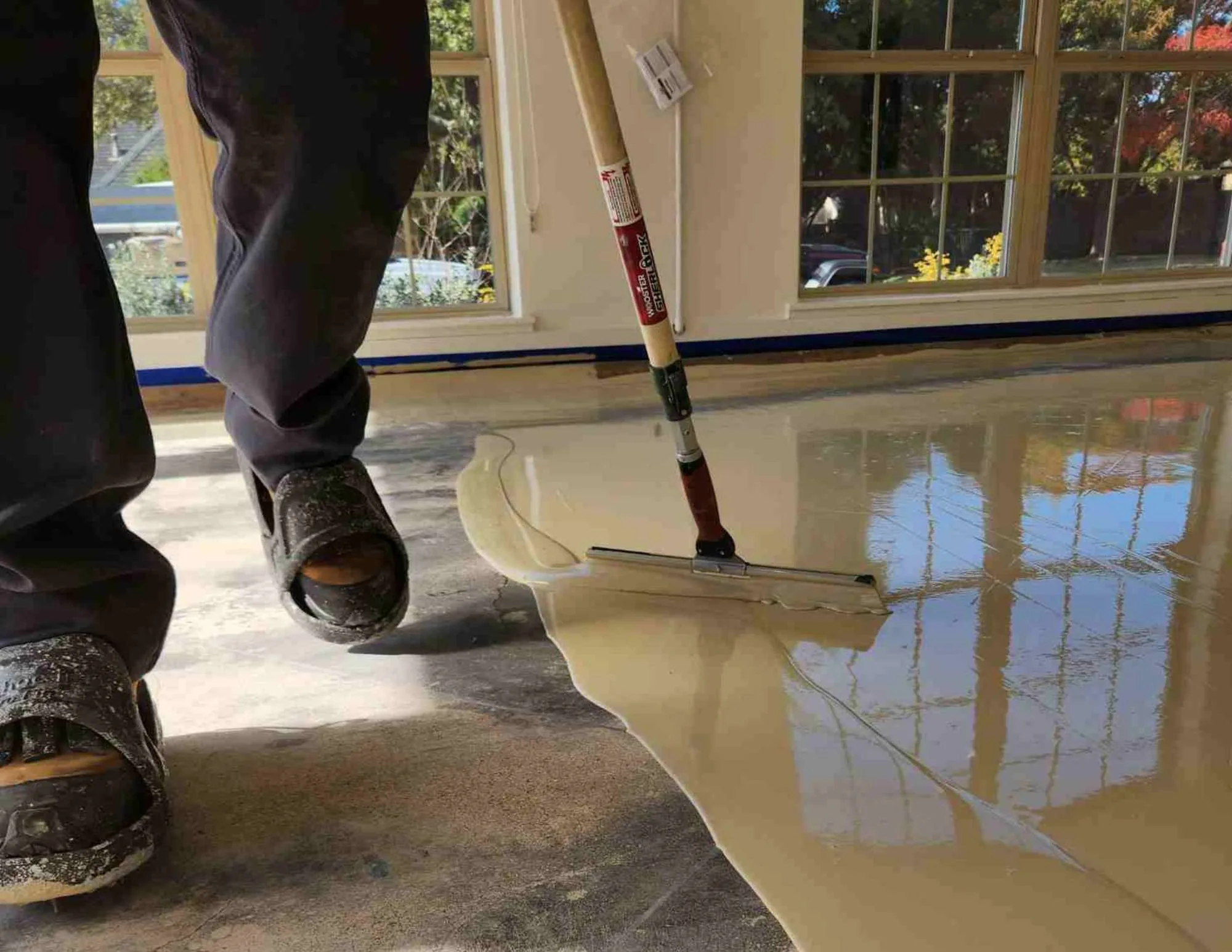 An installer spreading the base coat over bare concrete with a squeegee