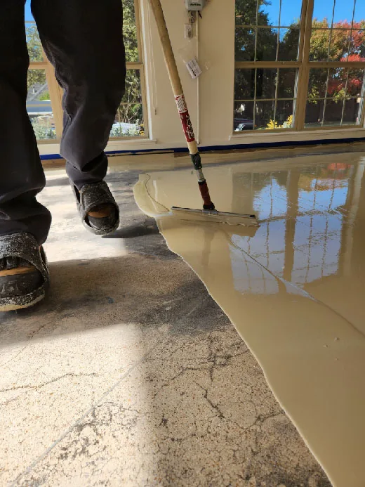 An installer spreading a pool of coating across a cracked concrete floor with a squeegee